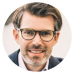 Man with glasses and beard smiling in a suit