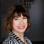 Woman with short brown hair and bangs smiles, wearing a polka dot top.
