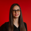 Woman with glasses and long dark hair smiles against red background