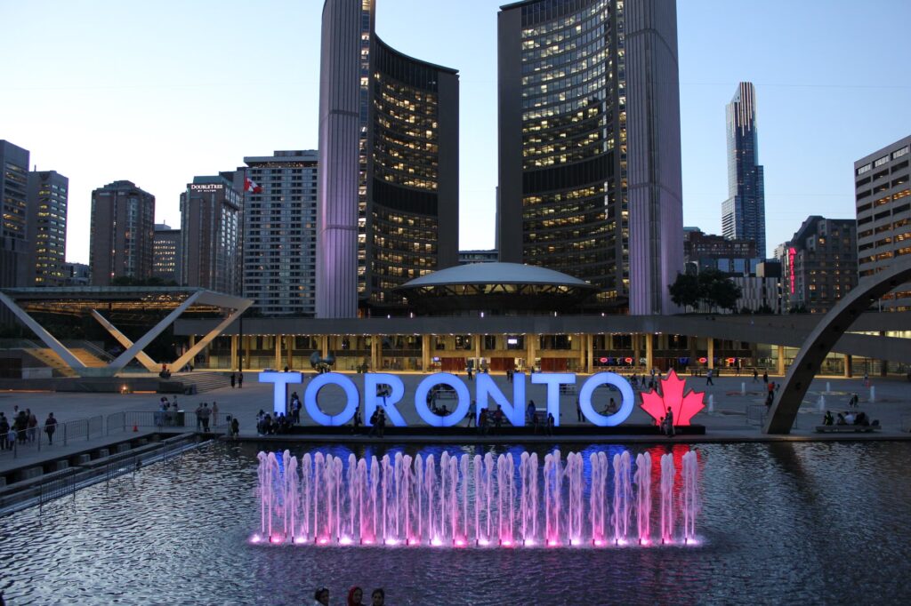 Twilight view of Toronto City Hall with vibrant fountain and prominent Toronto sign.