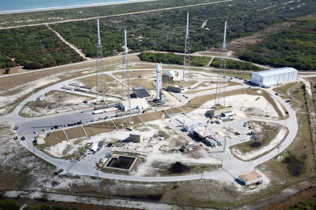 Drone view of spaceport with installed rocket ready for launching steel towers and hangar located amidst green f...