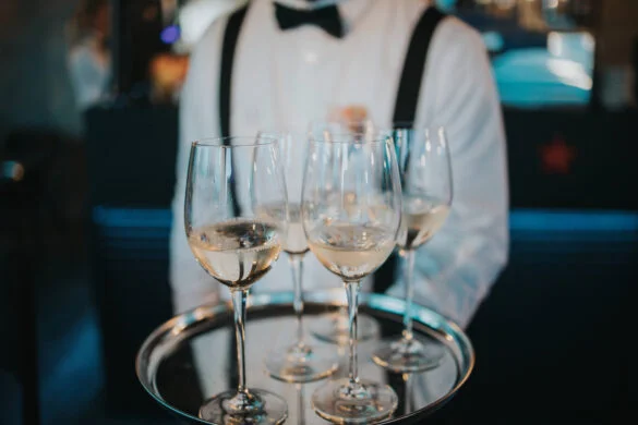 Waitperson in formal attire serving white wine in glasses on a silver tray